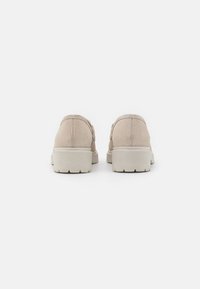Scarpe in suede beige con punta arrotondata e suola bassa e massiccia. Il retro presenta un design semplice e pulito con cuciture e texture sottili.