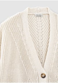 Kremowy kardigan dzianinowy z dekoltem w serek, zdobiony teksturowanymi wzorami, pojedynczym zapięciem na guzik oraz prążkowanymi wykończeniami wzdłuż krawędzi.