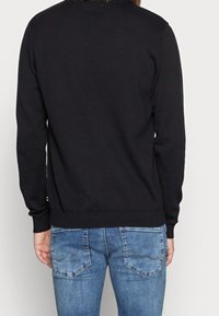 Maglione nero a maglia con maniche lunghe e polsini a costine, abbinato a jeans in denim blu chiaro con dettagli di cucitura sui taschini posteriori.