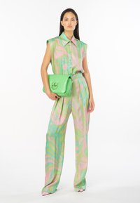 Canottiera verde senza maniche con motivi astratti rosa, abbinata a pantaloni larghi in colori simili. Completata da una borsa lucida verde.