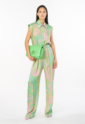 Canottiera verde senza maniche con motivi astratti rosa, abbinata a pantaloni larghi in colori simili. Completata da una borsa lucida verde.