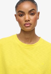Gul kortærmet sweatshirt med rund hals, lavet af blødt stof, med et diskret logo på brystet og en afslappet pasform.
