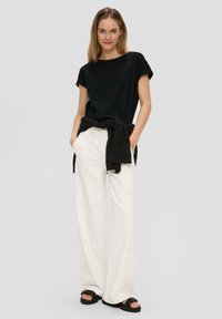 Czarna koszula z krótkim rękawem zestawiona z białymi szerokimi spodniami, podkreślona czarnym dzianinowym swetrem zawiązanym w talii oraz masywnymi czarnymi sandałami.