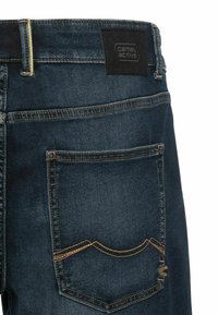 Mørkeblå denim jeans med gul syning, et mærke på taljebåndet og en baglomme med en buet søm og subtile detaljer.