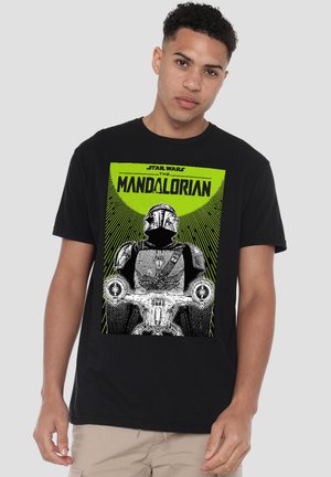 Mann trägt schwarzes T-Shirt mit The Mandalorian in Rüstung auf einem Speeder-Bike vor grünem Hintergrund und Star Wars-Schriftzug.
