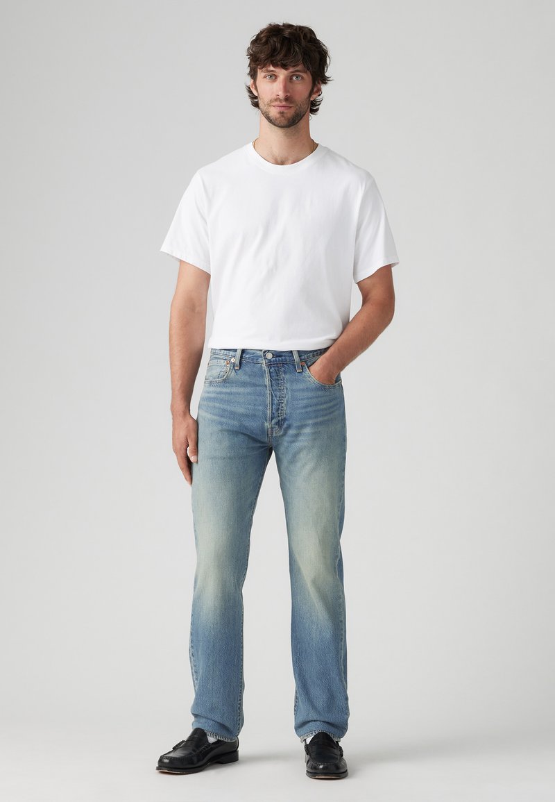 Jeans en denim bleu clair avec un effet usé, coupe droite, et cinq poches, associés à un t-shirt blanc à manches courtes.