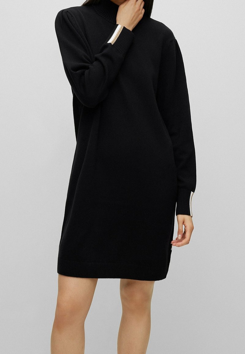 Robe en maille noire avec col montant, manches longues agrémentées d'accents argentés, et poignets et ourlet côtelés, offrant une coupe décontractée.