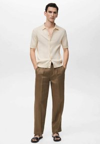 Short-sleeve, light beige ribbed shirt with buttons, paired with brown wide-leg trousers and black sandals. Simple design with a relaxed fit.