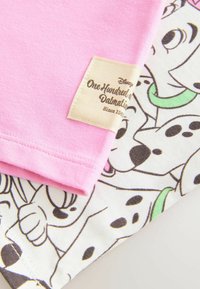 Różowa bawełniana tkanina z naszytą metką z napisem "Disney 101 Dalmatyńczyków". Biała tkanina poniżej ma wzory z dalmatyńczykami.