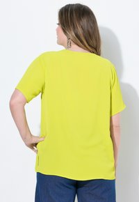 Maglietta a maniche corte di un vivace giallo, realizzata in tessuto leggero, con una vestibilità rilassata e spacco laterale, abbinata a pantaloni blu scuro.