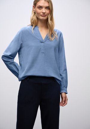 Hellblaue Bluse mit langen Ärmeln, V-Ausschnitt, lockerer Passform und gerafften Manschetten, kombiniert mit dunklen Hosen. Glatte Textur, minimalistisches Design.