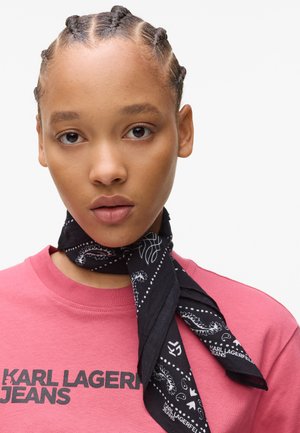 Black bandana scarf with white paisley pattern tied around the neck; worn with a pink t-shirt featuring bold black text "KARL LAGERFELD JEANS."