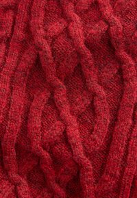 Tissu en laine rouge avec un motif en maille torsadée texturée, présentant des brins entrelacés qui créent une surface en relief avec profondeur et chaleur.