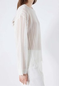 Pull léger et transparent blanc avec des rayures verticales, encolure ronde, poignets côtelés et détails d'ourlet non fini.