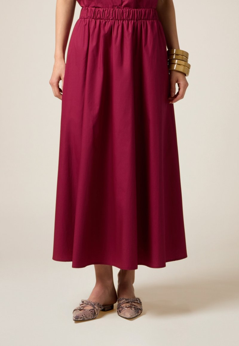 Larga falda fluida en magenta profundo, hecha de tela ligera con una cintura elástica. Combinada con zapatos planos de estampado serpiente.