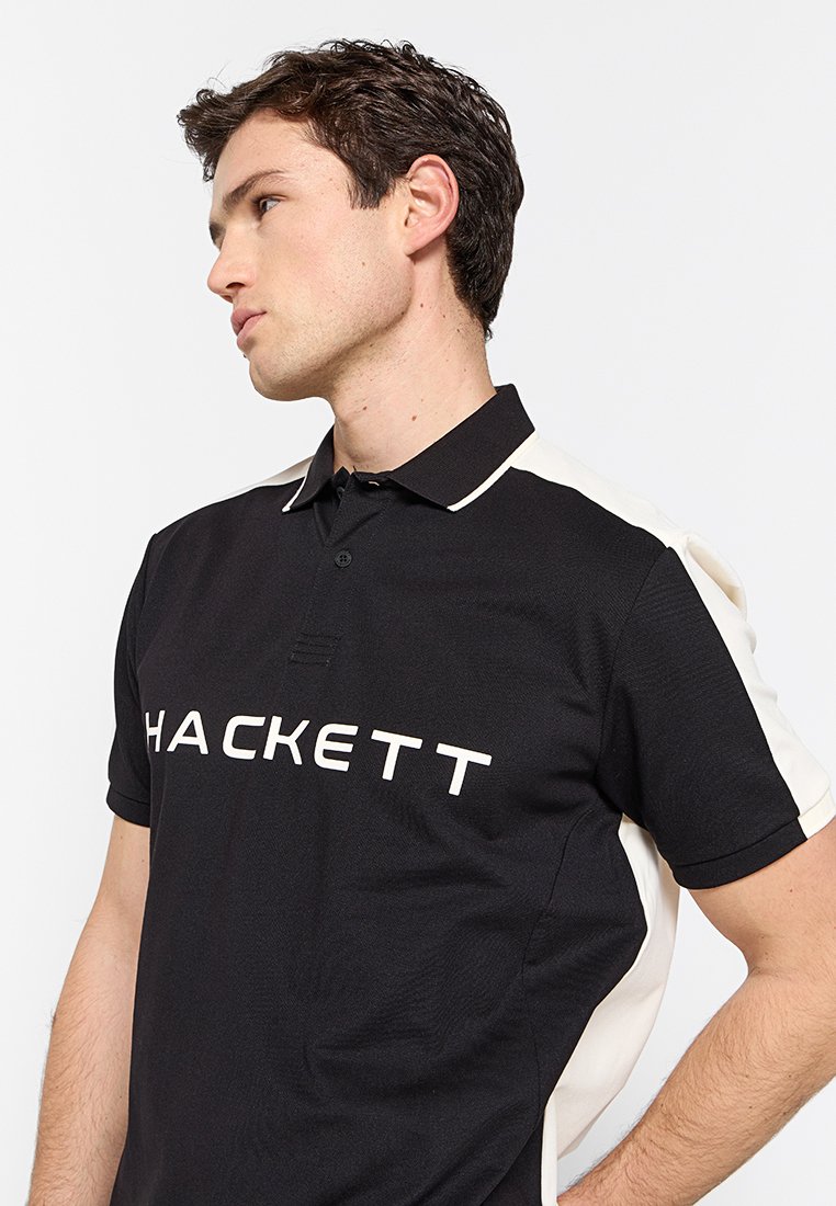 Schwarzes Polohemd mit cremefarbenen Seitenpanelen. Verfügt über einen mit Knöpfen versehenen Kragen und das "HACKETT"-Logo in Weiß auf der Vorderseite. Strukturierter Stoff.