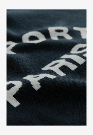 Tumed sinises kootud kangas, millel on tõstetud valged tähed, mis ütlevad "SPORT" ja "PARIS". Sile tekstuur kerge läikega.