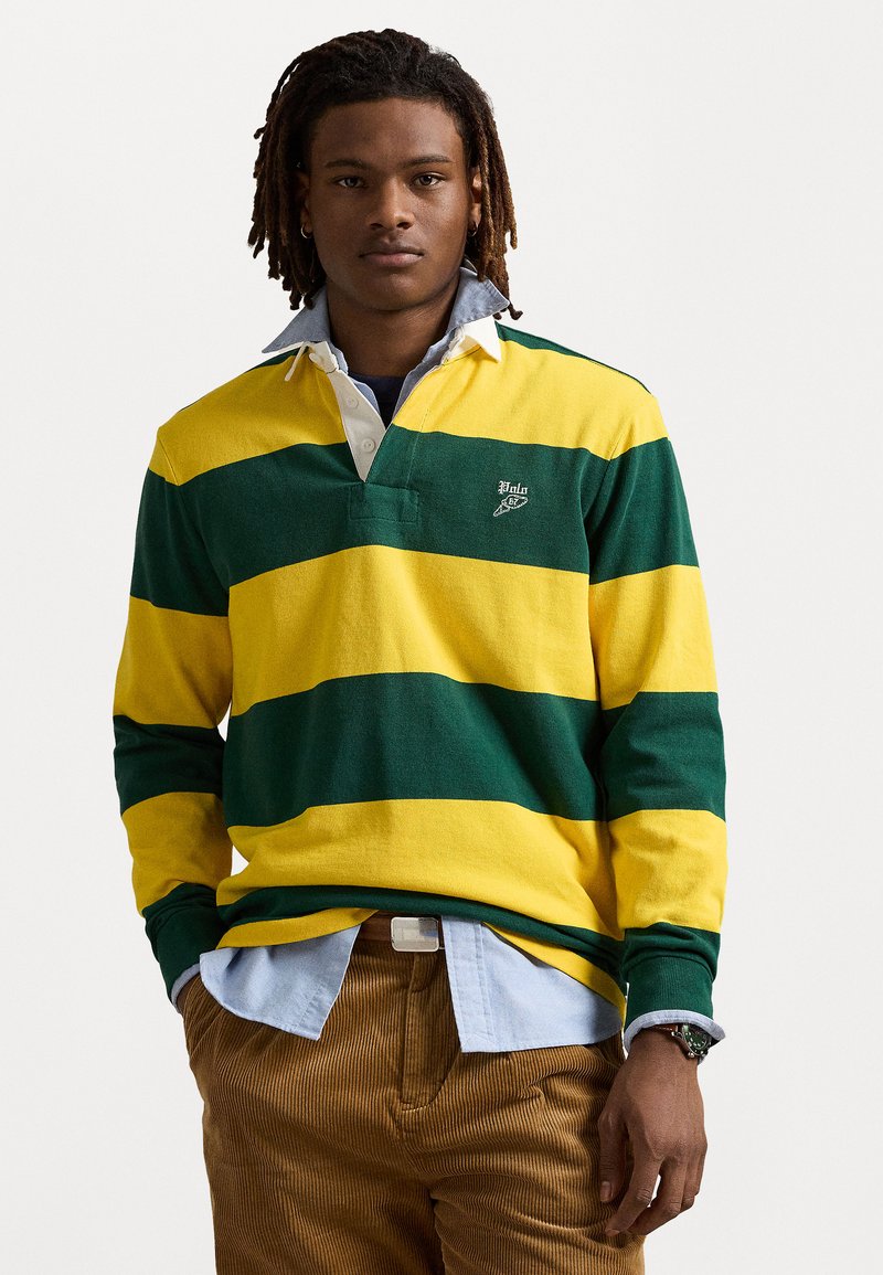 Groen en gele gestreepte polo met lange mouwen en een witte kraag, gecombineerd met een lichtblauw overhemd en een paar bruine corduroy broeken.