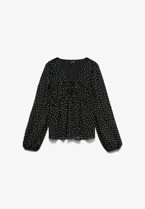 Blouse noire à manches longues avec pois blancs, col en V, détail froncé sur la poitrine et poignets élastiques aux manches.