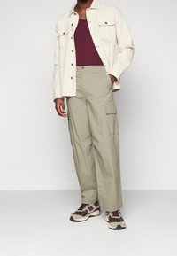 Krémová košile s knoflíky, bordó tílko, olivové cargo kalhoty a vícebarevné tenisky s akcenty na stranách a tkaničkami.