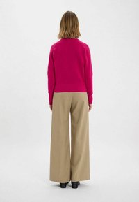 Pull en tricot fuchsia avec un col rond et un ourlet côtelé, associé à un pantalon beige à jambes larges et des bottes noires. Vue de dos.