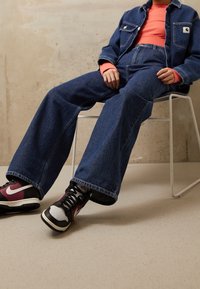 Jeansjacka och vida byxor i mörkblått, kombinerat med svarta och vinröda sneakers. Strukturerad tyg med en avslappnad passform.