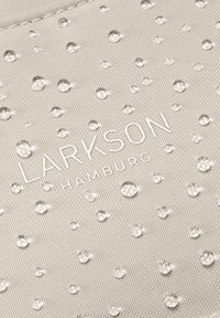 Gotitas de agua sobre tela beige texturizada con "LARKSON HAMBURG" impreso en letras blancas.