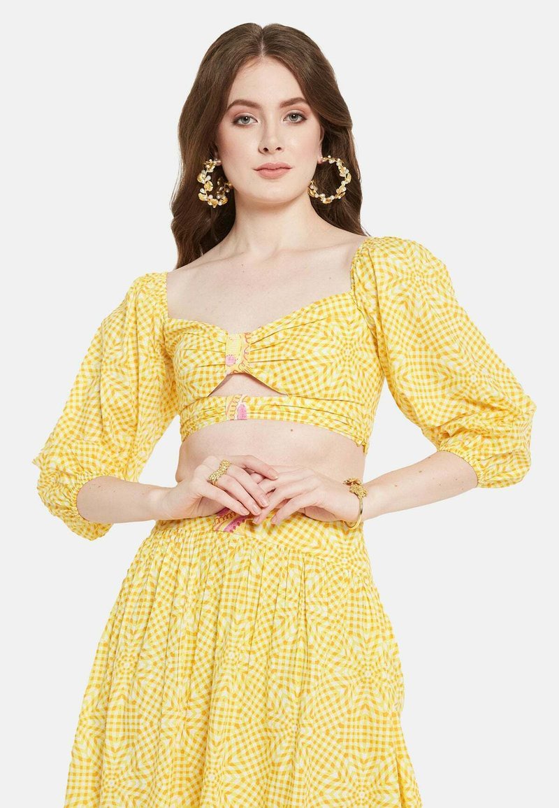 Completo a due pezzi giallo a quadretti, composto da un top corto con maniche a sbuffo e un dettaglio con apertura, abbinato a una gonna svasata coordinata.