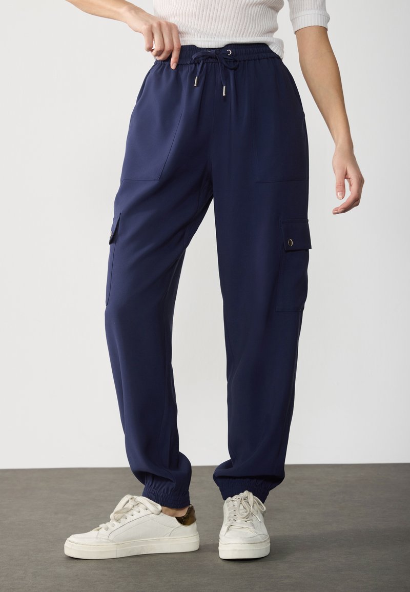 Pantaloni cargo blu navy realizzati in tessuto liscio con tasche laterali e polsini elasticizzati. Presentano una vita con cordoncino per una vestibilità regolabile.
