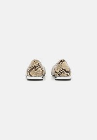 Slyngede skinnmønstrede slips-on sko med en beige base og brune detaljer. Har en lav profil og en hvit såle med svarte detaljer.