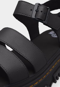 Μαύρο δερμάτινο σανδάλι με τρεις λουριά, ρυθμιζόμενο κούμπωμα και χοντρή σόλα με αυλακώσεις και κίτρινη ραφή.