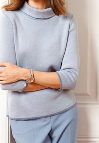 Suéter de punto azul claro con cuello alto y mangas tres cuartos, combinado con pantalones azul claro y un reloj de pulsera plateado.