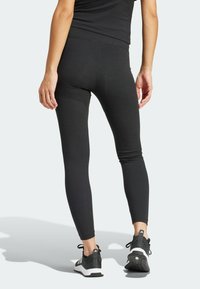 Leggings negras de canalé con cintura alta, con un corte ajustado y textura suave, combinadas con zapatos deportivos en negro y blanco.