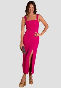 Vestido sin mangas fucsia con escote cuadrado, abertura lateral y diseño ajustado. Combinado con unos tacones de plataforma dorados y un bolso texturizado.