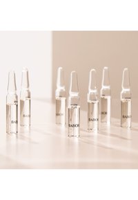 Ampoules en verre clair remplies de liquide, étiquetées "HYDRA PLUS" et "BABOR", disposées en rangée sur une surface claire.