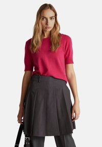 Fuchsia kurzer Pullover mit rundem Halsausschnitt, kombiniert mit einem dunkelgrauen, gefalteten Rock. Glatte Textur und maßgeschneiderte Passform.