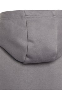 Felpa grigia con cappuccio, caratterizzata da un tessuto testurizzato, un cappuccio arrotondato e dettagli di cucitura visibili. Il materiale sembra morbido e resistente.