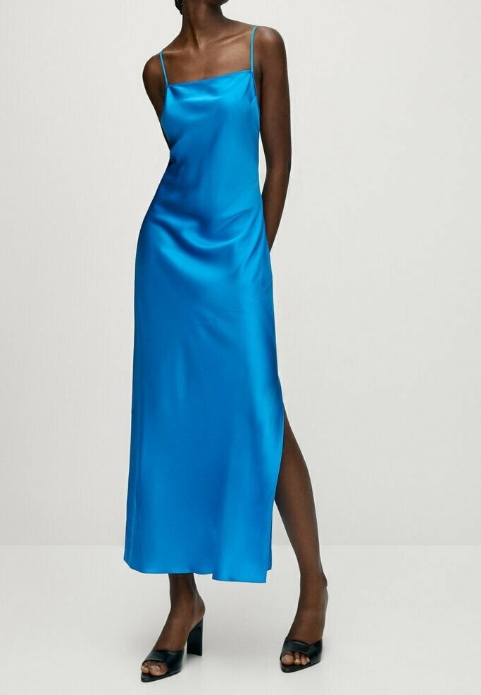Femme portant une robe nuisette en satin bleu vif avec fines bretelles et fente latérale, associée à des sandales noires à talons blocs et bout ouvert.