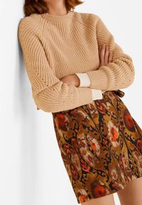 Beige neulepaita, jossa on ribbikuvio ja valkoiset yksityiskohdat, yhdistettynä ruskeaan kukkakuosiseksi hameeseen, jossa on oransseja ja mustia yksityiskohtia.