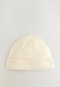 Cremefarbener, gerippter Strickbeanie mit umgeschlagenem Saum und einem kleinen gewebten Etikett an der Seite. Weiche Textur und schlankes Design.