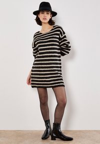 Strikket sweaterkjole med sorte og cremefarvede vandrette striber, oversized pasform, rund halsudskæring og trekvartærmer, parret med sorte ankelstøvler.