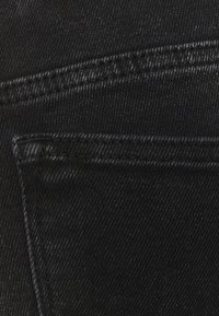 Tessuto in denim nero con vista ravvicinata di una tasca. La texture è liscia con una leggera lucentezza e cuciture a contrasto.
