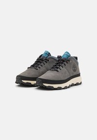 Zapatillas de senderismo de cuero gris con acentos negros y suelas texturizadas. Cordones azules y negros, cuello acolchado y detalle del logo en el lateral.