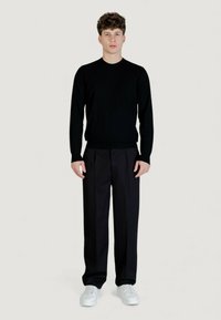 Maglione nero lavorato a maglia con collo tondo, abbinato a pantaloni scuri con pieghe. Indossato con sneakers bianche, creando un look monocromatico.