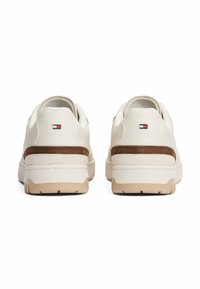 Sneaker bianche basso con suole beige e dettagli in suede marrone sul tallone, viste da dietro, con piccoli loghi rettangolari.