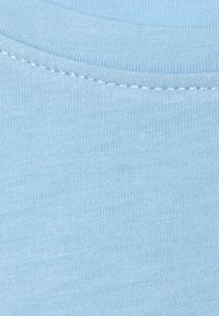 Light blue fabric with a smooth, knitted texture. Features a rounded neckline and fine stitching along the edges.
