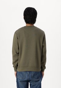 Sudadera verde oliva hecha de algodón, con un escote redondo, mangas largas y un corte relajado, combinada con jeans de mezclilla azules.