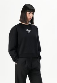 Zwarte sweatshirt met een ronde hals, lange mouwen en een verkorte pasvorm. Voorzien van de witte geborduurde tekst "Hugo" op de borst. Zachte textuur.