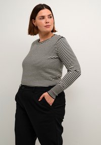 Zwart-wit gestreepte lange mouwen shirt met een ronde hals, gemaakt van een geribbeld materiaal. Gecombineerd met zwarte, op maat gemaakte, hoge taillebroeken.