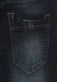 Jeans de mezclilla oscura con un bolsillo trasero de forma triangular, detalles de costura sutiles y una textura suave.